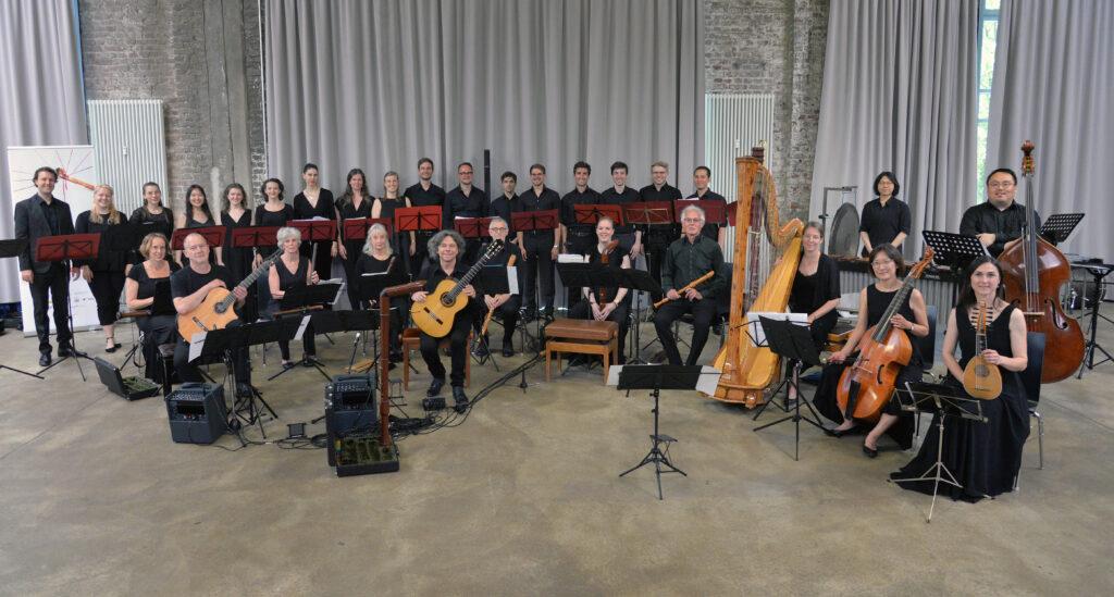 Bild eines Ensembles it verschiedenen Instrumenten, Gitarren, Flöten, Harfe, Streichinstrumente, alle schwarz gekleidet