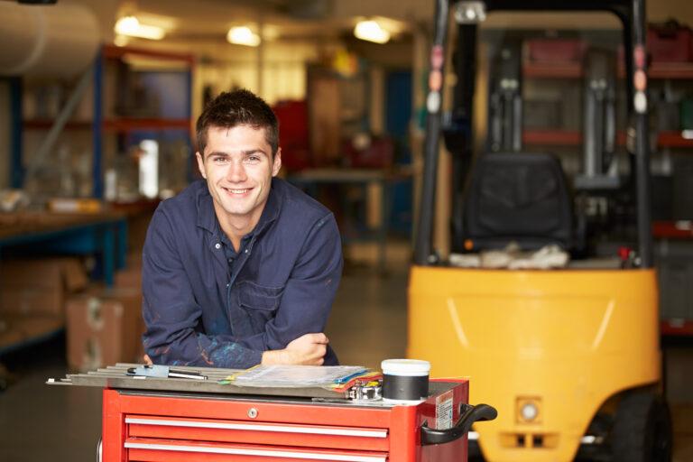 Porträt eines angehenden Ingenieurs in einer Fabrik, der in die Kamera lächelt.